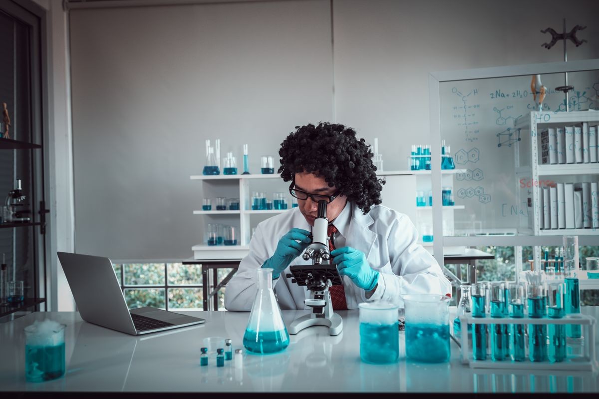 Professor with curly hair working at the research center using a microscope. chemists working with blue liquids in tubes at The Chemical Research Lab.